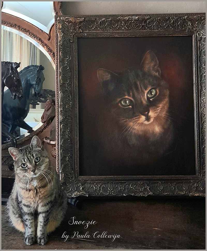 kat poseert bij schilderij met een portret van de kat. het schilderij is ingelijst.